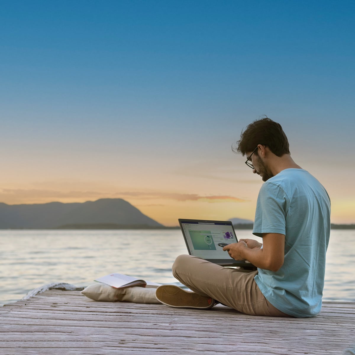 Person sitting on pier with laptop open.